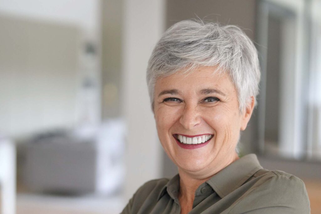 Χαμογελαστή γυναίκα με φυσικά δόντια, επιδεικνύοντας την αποτελεσματικότητα της προσθετικής δοντιών.